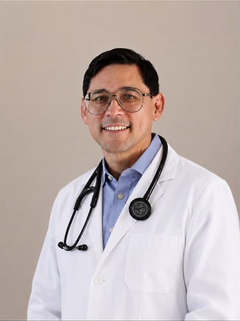 Portrait of a smiling male doctor wearing glasses, white lab coat, and stethoscope against a neutral background